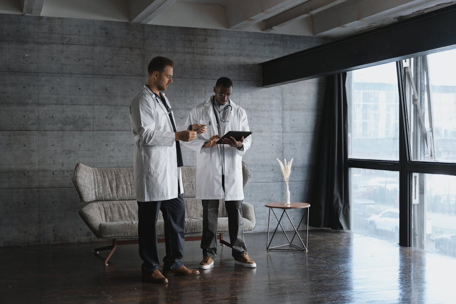 Two doctors in an industrial office discuss patient data on a digital tablet.